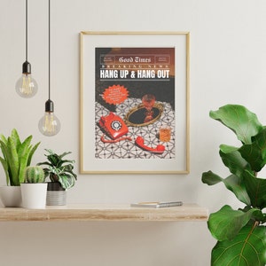May include: A gold framed print with the text "Good Times Breaking News Hang Up & Hang Out" and a red rotary phone with a glass of liquid on a tray. The print is on a white wall with a shelf below it.