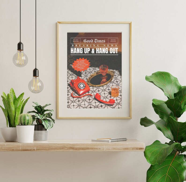 May include: A gold framed print with the text "Good Times Breaking News Hang Up & Hang Out" and a red rotary phone with a glass of liquid on a tray. The print is on a white wall with a shelf below it.