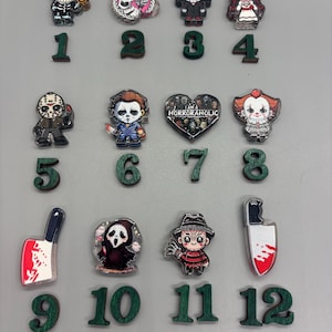 May include: A collection of twelve horror-themed acrylic charms arranged in three rows, each labeled with a green wooden number from 1 to 12. The charms feature various iconic characters and symbols, including a heart-shaped piece with the text I AM A HORRORAHOLIC.