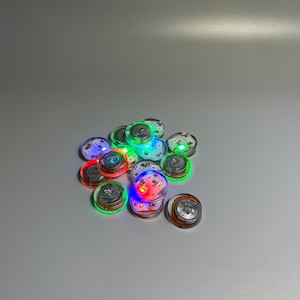May include: A group of small, round, clear plastic buttons with embedded LED lights. The lights are in various colors, including red, green, blue, and white.