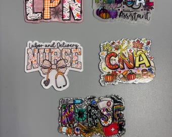 May include: A collection of five decorative badge reels for medical professionals. The badges feature various designs, including the text "LPN", "Medical Assistant", "Labor and Delivery Nurse", "CNA", and "Nurse". Each badge has a unique design with Halloween and fall themes.