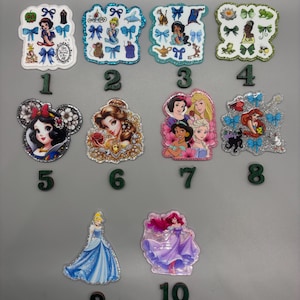 May include: A collection of ten glittery, decorative stickers featuring various princess characters. The stickers are in different shapes and sizes, with vibrant colors and detailed designs. Each sticker has a number from 1 to 10.