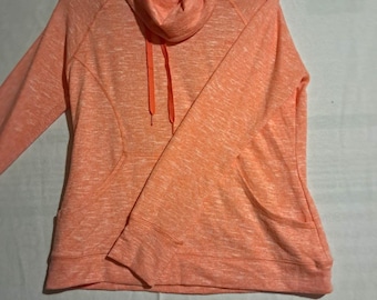 May include: A long-sleeve pullover sweatshirt in a heathered coral orange colour. It features a cowl neckline with matching orange drawstrings, raglan sleeves, and two front pockets integrated into the side seams of the garment.