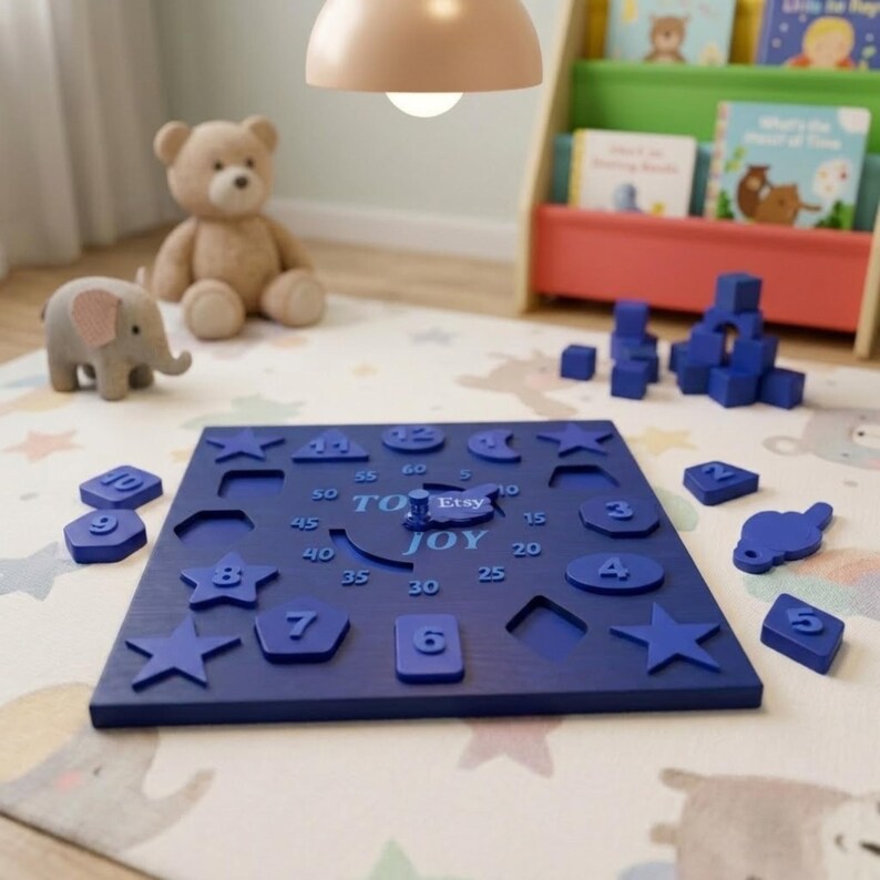 May include: A dark blue wooden square puzzle board featuring cutouts for various shapes and numbers. The board displays the text TOY JOY and Etsy in the centre, with numbers 5 through 60 printed in increments of 5 around a central clock hand.