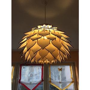 Könnte beinhalten: Eine hölzerne Pendelleuchte mit einem einzigartigen Design, das an eine Blütenknospe erinnert. Die Leuchte besteht aus vielen einzelnen Holzstücken, die in einem kreisförmigen Muster angeordnet sind. Die Leuchte ist beleuchtet und strahlt ein warmes Licht aus.