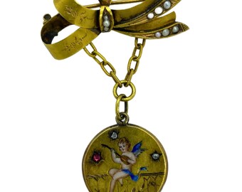 May include: A gold tone brooch with a pearl-encrusted bow and a dangling charm featuring a painted cherub playing a lute. The charm is surrounded by a gold tone frame and has a red and blue enamel design.