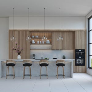 Puede incluir: Interior de cocina moderno con gabinetes de madera clara, una isla de encimera de mármol con cuatro taburetes de bar y luces colgantes. También se ve un horno empotrado y una ventana grande. Un jarrón de flores rosas añade un toque de color.