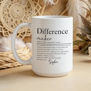 May include: White ceramic mug with the text "Difference maker" and a definition. The mug also includes the name "Sophia". The mug has a large handle and is surrounded by decorative elements.
