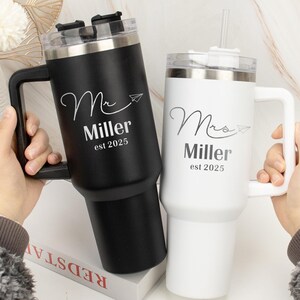 Pu&ograve; includere: Due tazze da viaggio in acciaio inox con manici. La tazza nera dice "Mr. Miller est 2025" e la tazza bianca dice "Mrs. Miller est 2025".