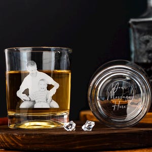 Könnte beinhalten: Ein klares Whiskyglas mit einem Foto von Vater und Kind auf der Vorderseite, gefüllt mit bernsteinfarbener Flüssigkeit. Der Boden eines zweiten Glases zeigt den Text "Your Message Here". Die Gläser stehen auf einem Holzuntersetzer.