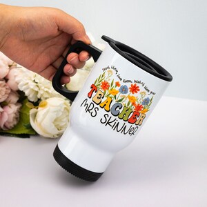 May include: White travel mug with a black handle and lid. The mug features the text "TEACHER MRS SKINNER" in colorful letters, surrounded by floral illustrations. The words "Teach them, love them, watch them grow" are also printed on the mug.