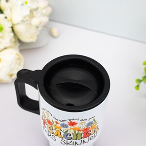 May include: White travel mug with a black handle and lid. The mug features a floral design with the words "Teacher Mrs. Skinner" in colorful, retro-style lettering. The text "with them, love them, watch them grow" is also included.