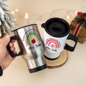 Puede incluir: Dos tazas de viaje, una de acero inoxidable y otra blanca, con asas y tapas negras. Cada taza presenta un dise&ntilde;o de arco&iacute;ris con una manzana o frambuesa, el texto "It takes a big heart to shape little minds" y el nombre "Mrs. Smith."