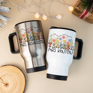May include: Two travel mugs with black handles. One is silver, the other white. Both have the word "TEACHER" in colorful letters, floral designs, and the names "MRS. RICHARDSON" and "MRS KENTON". The text "Teach them, love them, watch them grow" is also present.