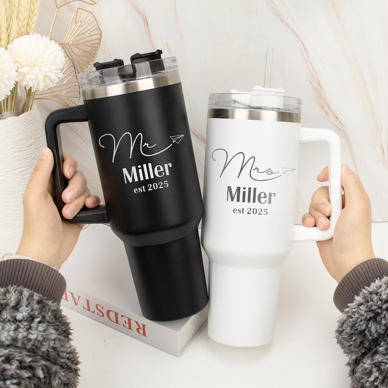 Pu&ograve; includere: Due tazze da viaggio in acciaio inox con manici. La tazza nera dice "Mr. Miller est 2025" e la tazza bianca dice "Mrs. Miller est 2025".
