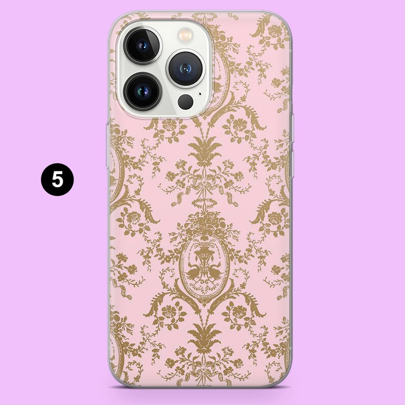 May include: A pink phone case with a gold floral damask pattern. The case has a clear border and features a camera cutout. The number "5" is in a black circle in the upper left corner.