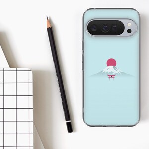 May include: A light blue phone case with a minimalist design of a mountain, a red sun, and a Japanese torii gate. A black pencil and a white notebook with a grid pattern are also visible.