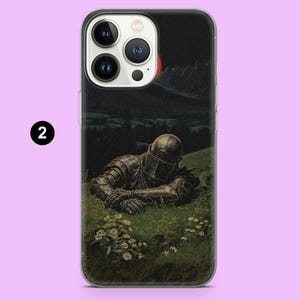 May include: A phone case featuring a painting of a knight in full armor resting in a grassy field. The artwork has a dark, dramatic tone with a night sky and distant mountains. The case is clear with a black number 2 in the corner.