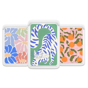 Puede incluir: Tres tarjeteros blancos para teléfono con diseños coloridos. Uno presenta flores azules y rosas, otro un gato azul y blanco sobre verde, y el último naranjas y hojas sobre rosa. Los tarjeteros son rectangulares con esquinas redondeadas.
