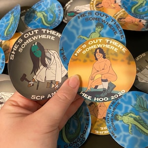 May include: A collection of round stickers with colorful backgrounds and illustrations. The stickers feature various characters and text, including "He's Out There Somewhere", "She's Out There Somewhere", and "Hee Hoo 2020".