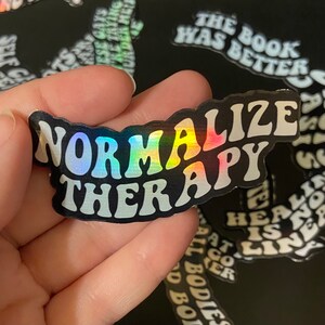 May include: A black and white sticker with iridescent rainbow foil lettering that reads "Normalize Therapy".