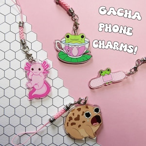 Puede incluir: Colección de colgantes para teléfono Gacha con diseños de animales. Incluye un ajolote rosa, una rana en una taza de té, una rana en una tirita y una rana llorando. Cada colgante tiene un cordón rosa.