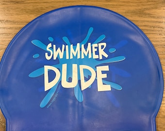 May include: Blue silicone swim cap with a white splatter design and the text "Swimmer Dude" and "www.tagoggles.com".