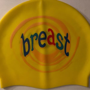 May include: Yellow swim cap with the word "breast" in colorful letters. The word is surrounded by a spiral design in orange and light orange. The swim cap is made of a smooth, flexible material.