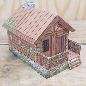 Pode incluir: Uma cabana de papel com varanda, com telhado e paredes castanhas, pequenas janelas e uma chaminé de pedra. O texto "Log cabin with front porch" e "Digital Download" são visíveis.