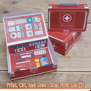 May include: Printable miniature first aid kit, red and white, with a cross and the words "First Aid Box". The kit is open and shows the inside with various medical supplies, including bandages, pills, and a thermometer.