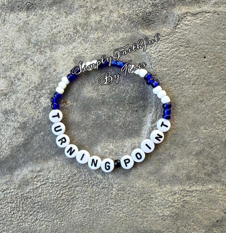 May include: A bracelet made of white letter beads spelling "TURNING POINT", interspersed with blue and white beads. The text "Simply Faithful By Rois" is written in cursive above the bracelet.