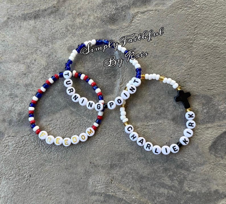 May include: Three beaded bracelets with white letter beads spelling "FREEDOM", "TURNING POINT", and "CHARLIE KIRK". The bracelets feature red, white, and blue beads, and gold-coloured beads. The bracelets are on a grey surface. The text "Simply Faithful By Kris" is in the background.