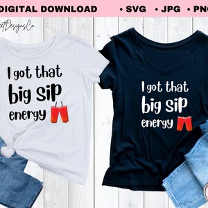 May include: Two t-shirts, one white and one navy blue, each with the phrase "I got that big sip energy" in black text. The design includes a graphic of two red drinks with straws. The shirts are paired with blue jeans.
