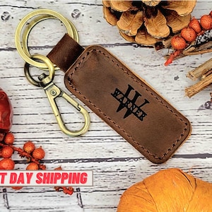 May include: Brown leather keychain with a gold metal key ring and a personalized monogram. The monogram is in black and reads "Warner".