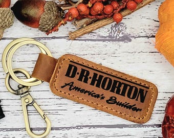 May include: A brown leather keychain with a gold metal key ring and a metal clasp. The keychain has the text "D.R. Horton America's Builder" embossed in black.