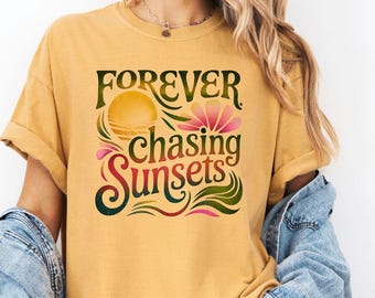 May include: Mustard-colored t-shirt with the text "FOREVER chasing SUNSETS" in a decorative font. The design includes a sun, flower, and flowing lines in shades of green, pink, and orange. The model is wearing a denim jacket.