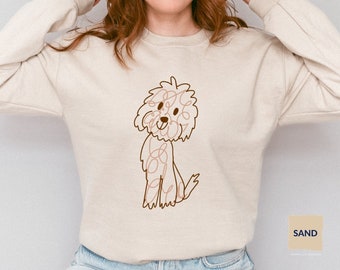 May include: A beige sweatshirt with a brown line drawing of a dog on the front. The dog is sitting and has a curly tail. The sweatshirt has a crew neck and long sleeves.