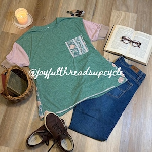 May include: A green t-shirt with pink sleeves and a floral pocket, paired with blue jeans and brown sneakers. An open book with glasses, a candle, and a basket with books are also in the image. The text "@joyfulthreadsupcycle" is visible.