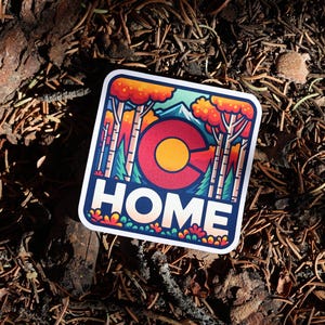 May include: A square sticker with rounded corners featuring a colorful illustration of a forest with orange and green trees, a mountain peak, and the letter C in red and yellow, with the word HOME printed in bold white capital letters below.