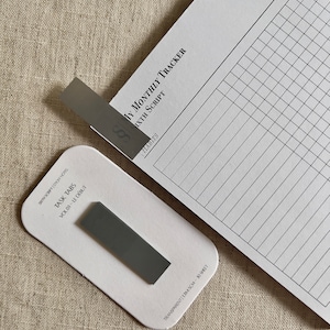 May include: A set of gray task tabs with the text "SIXTH SCRIPT STICKY NOTES" and "TASK TABS" on the front. The tabs are labeled "VOL. 01 - LE DÉBUT".
