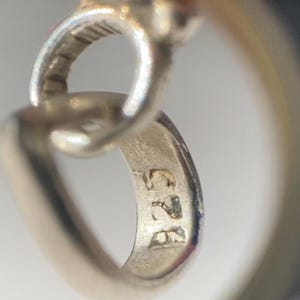 Peut inclure: Gros plan d'un pendentif en argent avec une pierre pr&eacute;cieuse verte. Le pendentif a une boucle pour l'attacher &agrave; une cha&icirc;ne et est marqu&eacute; du num&eacute;ro "925" au dos.