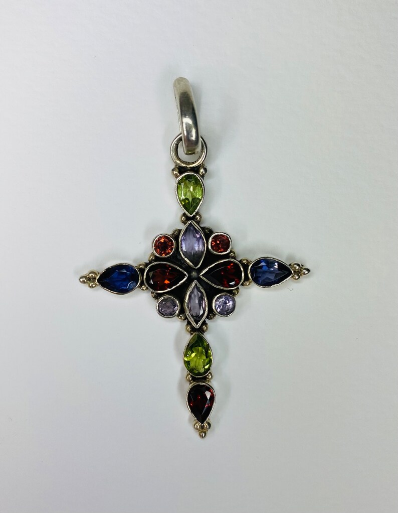 Peut inclure: Un pendentif en argent en forme de croix avec un motif floral orn&eacute; de pierres pr&eacute;cieuses vari&eacute;es, dont de l'am&eacute;thyste, du grenat, du p&eacute;ridot et du saphir.