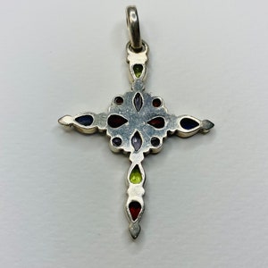 Peut inclure: Un pendentif en forme de croix en argent avec des pierres pr&eacute;cieuses color&eacute;es. La croix est d&eacute;cor&eacute;e de pierres pr&eacute;cieuses rouges, vertes, violettes et bleues.