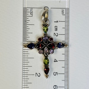 Peut inclure: Un pendentif en forme de croix en argent avec un design de pierres pr&eacute;cieuses multicolores. La croix mesure environ 4,5 cm de haut et pr&eacute;sente des pierres pr&eacute;cieuses rouges, vertes, violettes et bleues.
