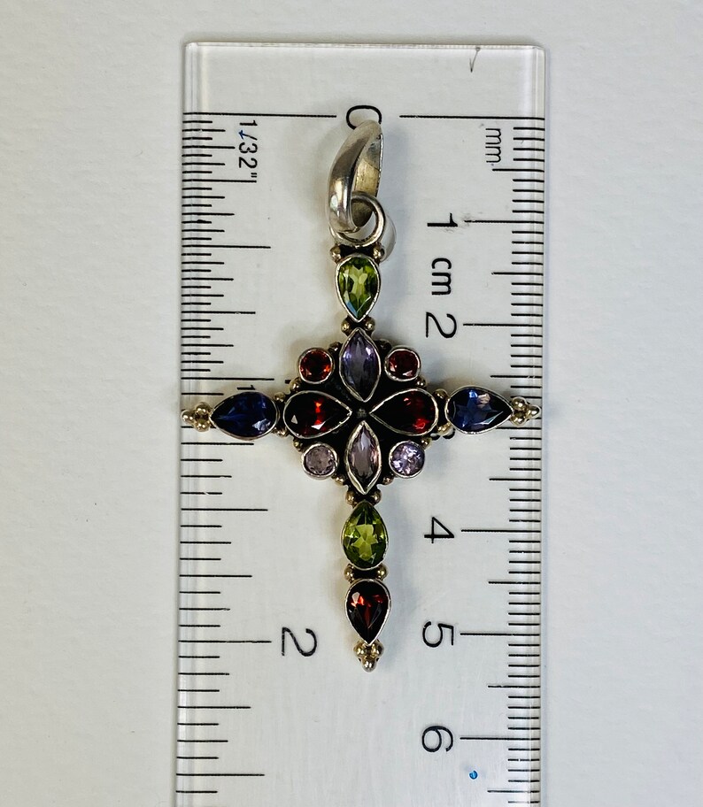 Peut inclure: Un pendentif en forme de croix en argent avec un design de pierres pr&eacute;cieuses multicolores. La croix mesure environ 4,5 cm de haut et pr&eacute;sente des pierres pr&eacute;cieuses rouges, vertes, violettes et bleues.