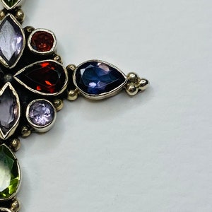 Peut inclure: Un pendentif en argent avec un motif floral orn&eacute; de pierres pr&eacute;cieuses de diff&eacute;rentes couleurs, notamment du vert, du violet et du rouge.