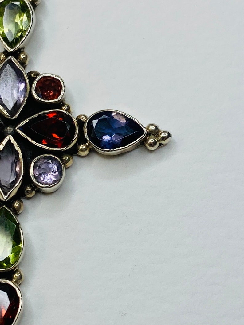 Peut inclure: Un pendentif en argent avec un motif floral orn&eacute; de pierres pr&eacute;cieuses de diff&eacute;rentes couleurs, notamment du vert, du violet et du rouge.