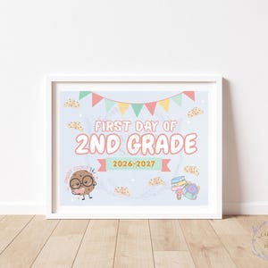 Peut inclure: Une affiche encadrée sur fond bleu clair avec des fanions colorés, le texte "FIRST DAY OF 2ND GRADE 2026-2027", un personnage de biscuit portant des lunettes avec l'inscription "SMART COOKIE", ainsi que des illustrations de livres et un sac à dos.