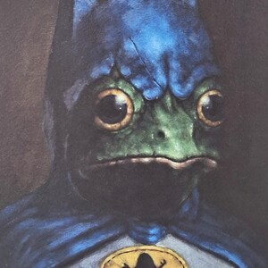 May include: A whimsical illustration of a frog dressed as Batman. The frog has a green face, large yellow eyes, and a blue cowl. A yellow emblem with a frog silhouette is on the chest. The artwork has a painterly style.