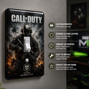 Pode incluir: Tampa de interruptor de luz preta com um soldado do videogame Call of Duty. A tampa tem o logotipo do jogo e o texto "Victory Belongs to Us". O interruptor é branco.